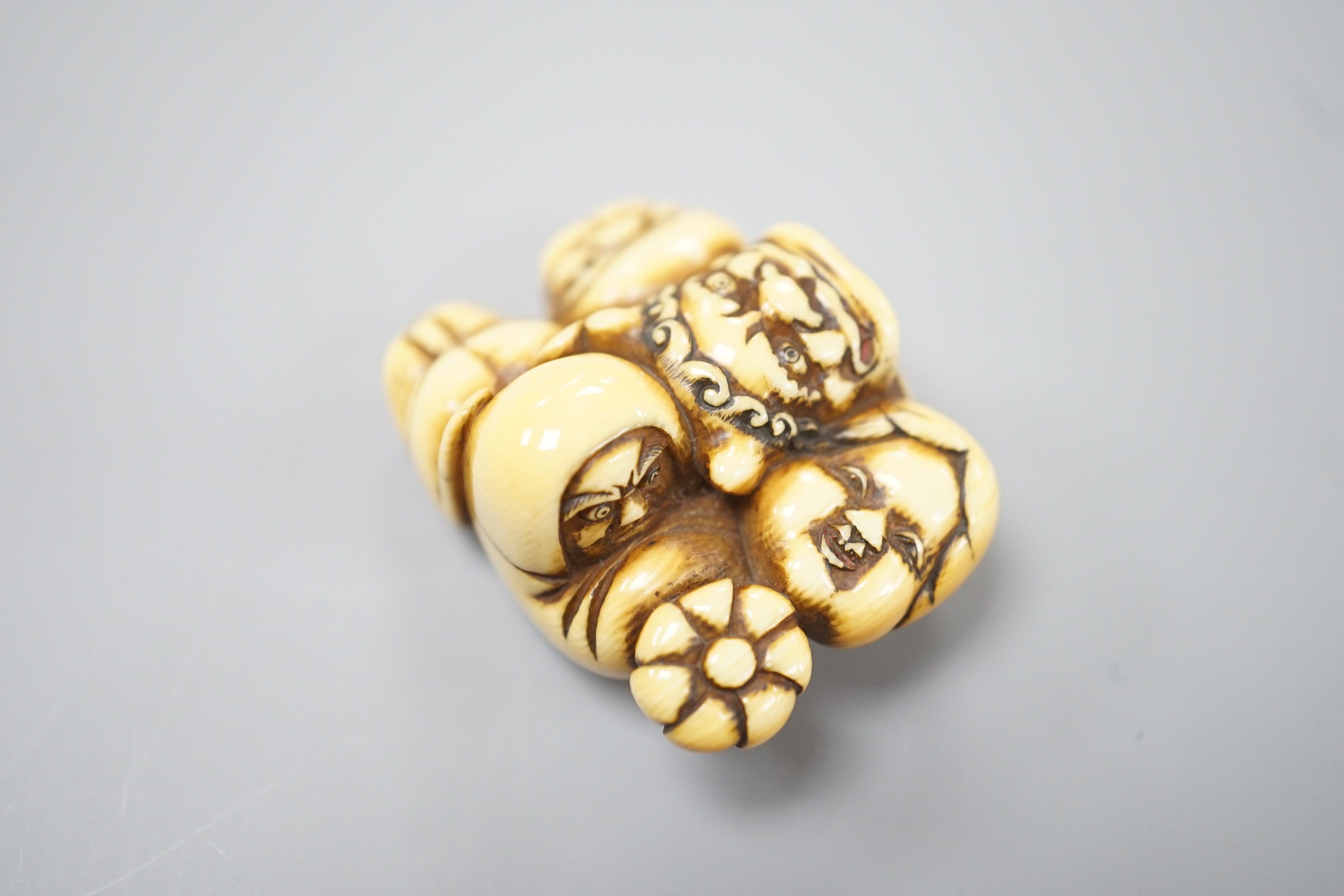 A Japanese ivory netsuke of a Daruma doll and four noh masks, signed, 19th century, 3.8cm